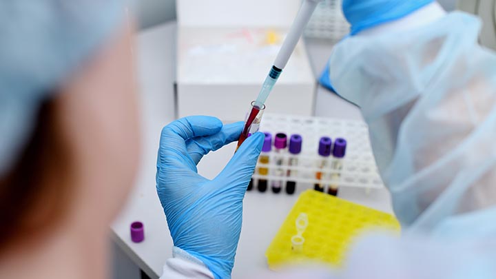 A lab technician pipetting a sample into a test tube.