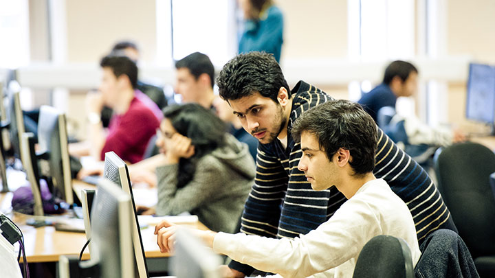 Students working at a computer within a computer lab.
